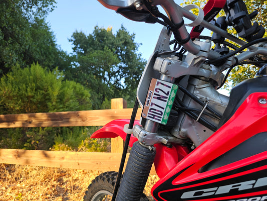Close-up of a red dirt bike with a off highway registration license plate sticker mount in an outdoor setting