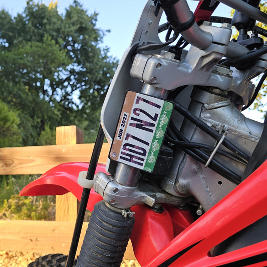 Close-up of a red dirt bike with a off highway registration license plate sticker mount in an outdoor setting