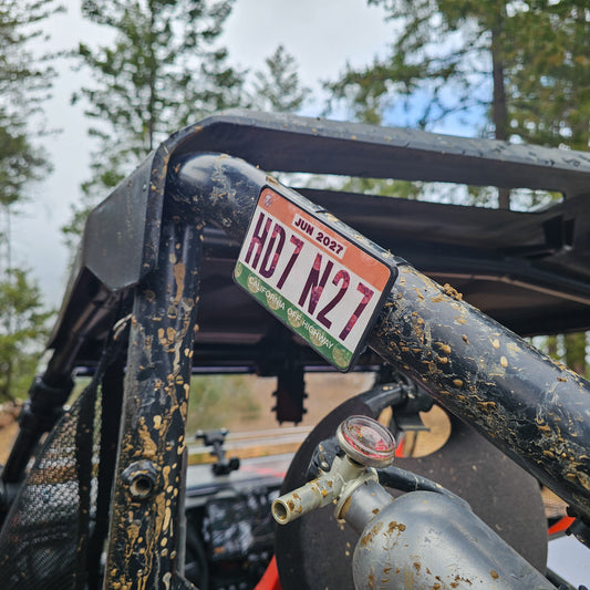 Close-up of a red UTV or Side by Side (SxS), or RZR with a off highway registration license plate sticker mount in an outdoor setting splattered with mud