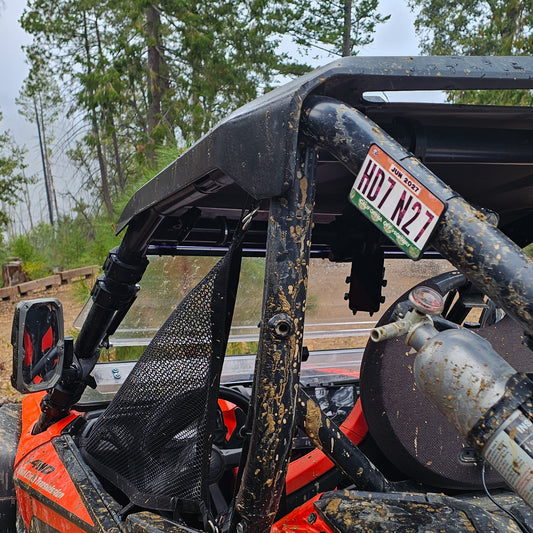 Close-up of a red UTV or Side by Side (SxS), or RZR with a off highway registration license plate sticker mount in an outdoor setting splattered with mud