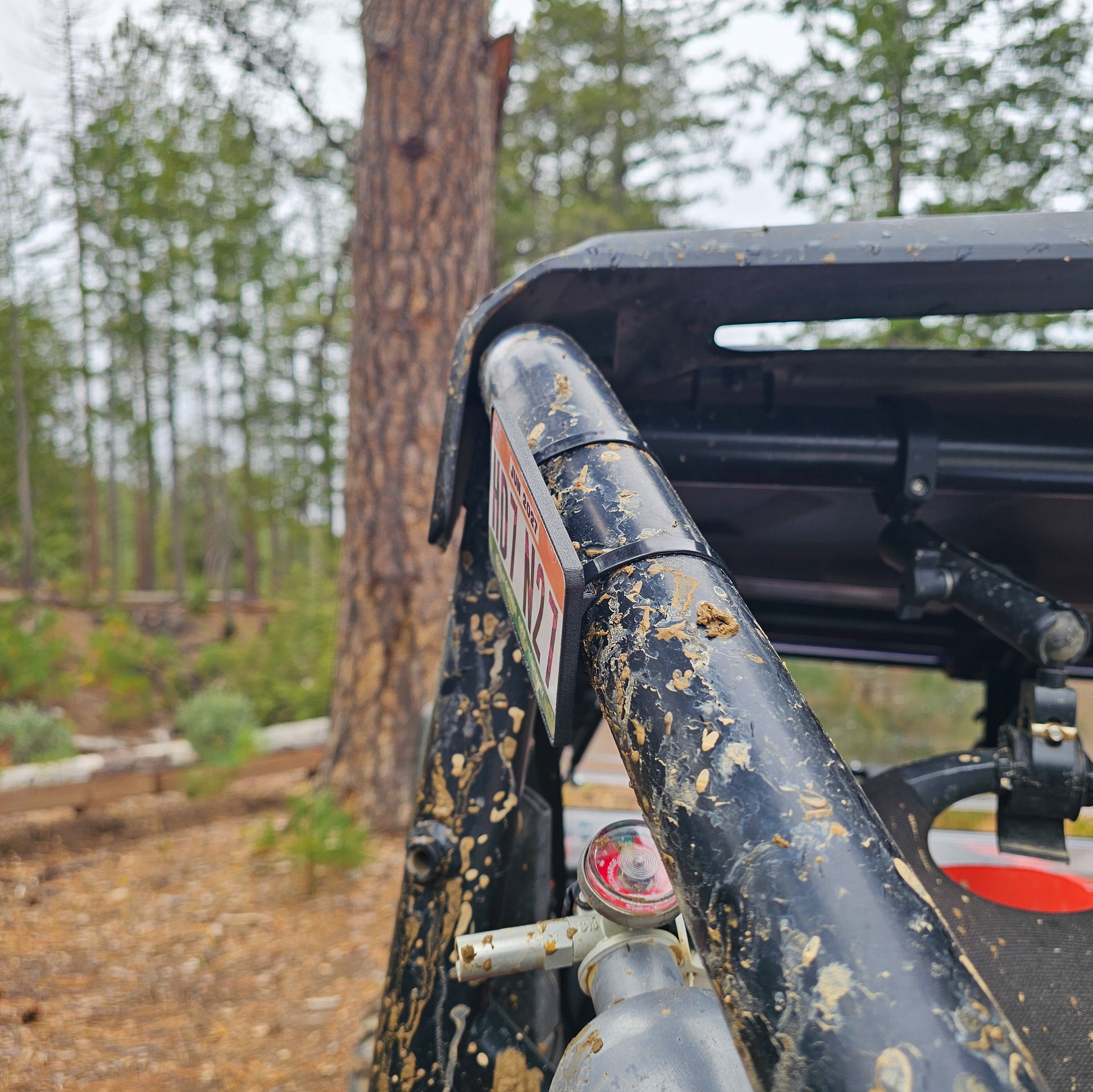 Close-up of a red UTV or Side by Side (SxS), or RZR with a off highway registration license plate sticker mount in an outdoor setting splattered with mud 