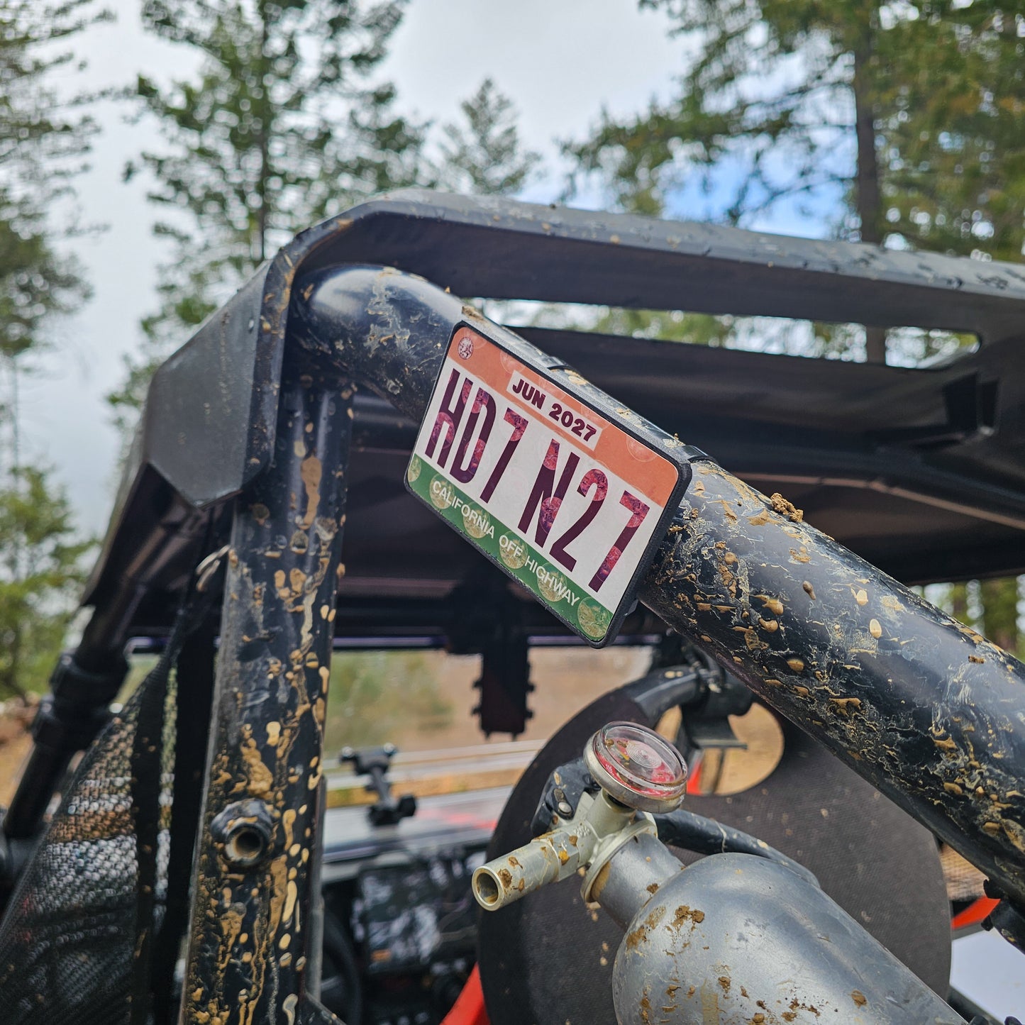Close-up of a red UTV or Side by Side (SxS), or RZR with a off highway registration license plate sticker mount in an outdoor setting splattered with mud 