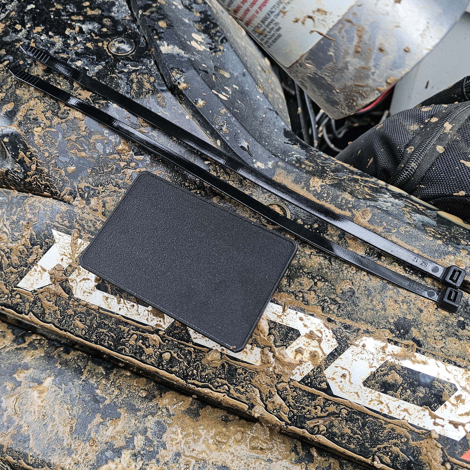 Close-up of a off highway registration license plate sticker mount for UTVs, RZRs, or Side by Side (SxS) in an outdoor setting splattered with mud 