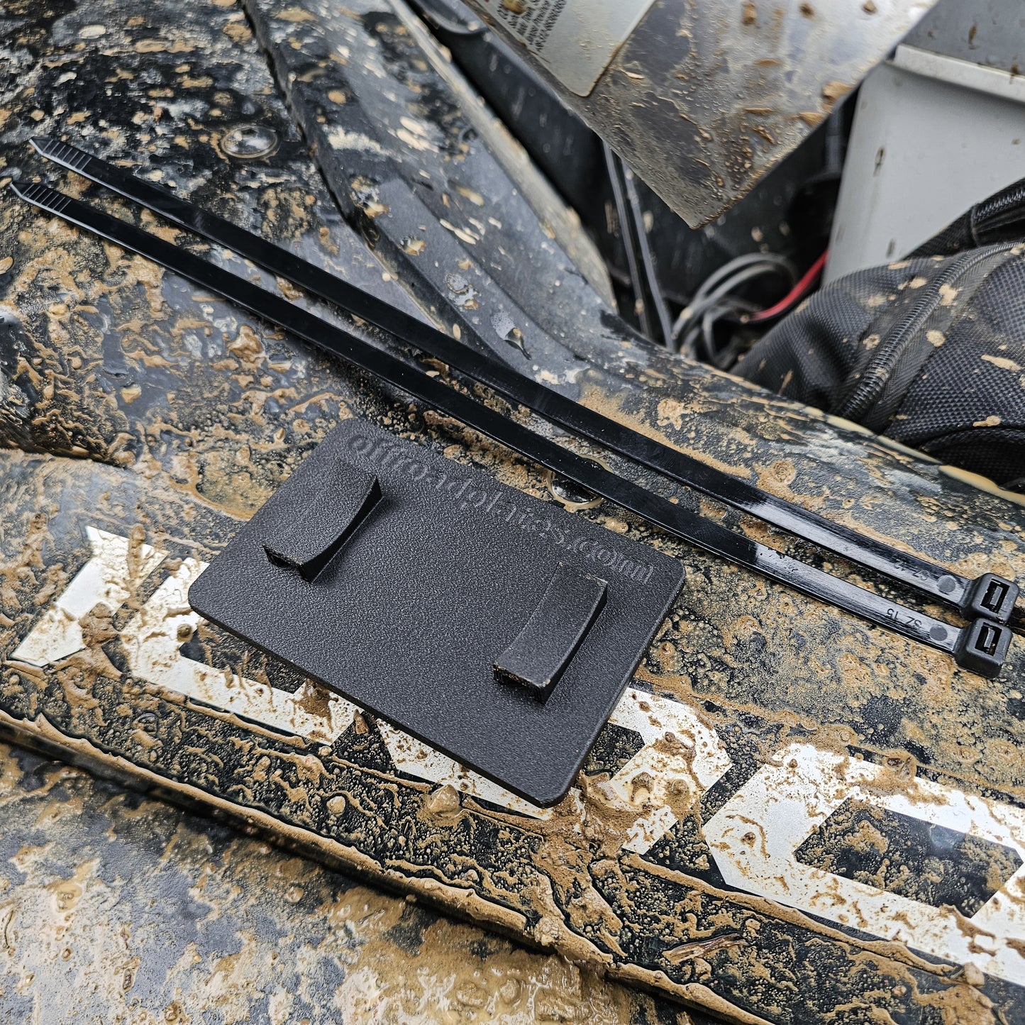 Close-up of a off highway registration license plate sticker mount for UTVs, RZRs, or Side by Side (SxS) in an outdoor setting splattered with mud.